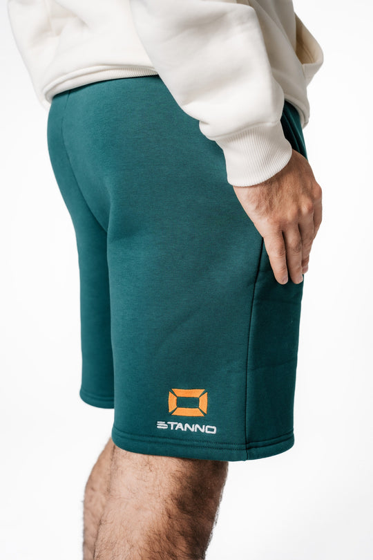 Detailaufnahme der dunkelgrünen POWWOW Team Shorts, die das gestickte orangefarbene Stanno-Logo auf dem rechten Bein zeigt.
