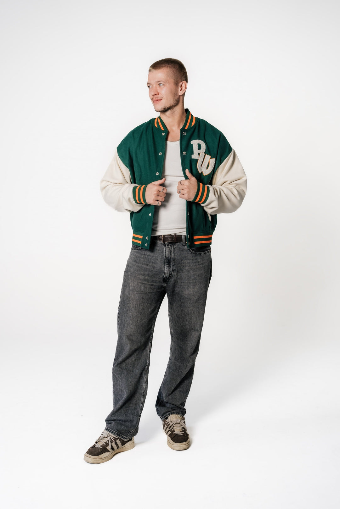 Männliches Model steht und trägt die offene grüne POWWOW College-Jacke mit cremefarbenen Ärmeln.