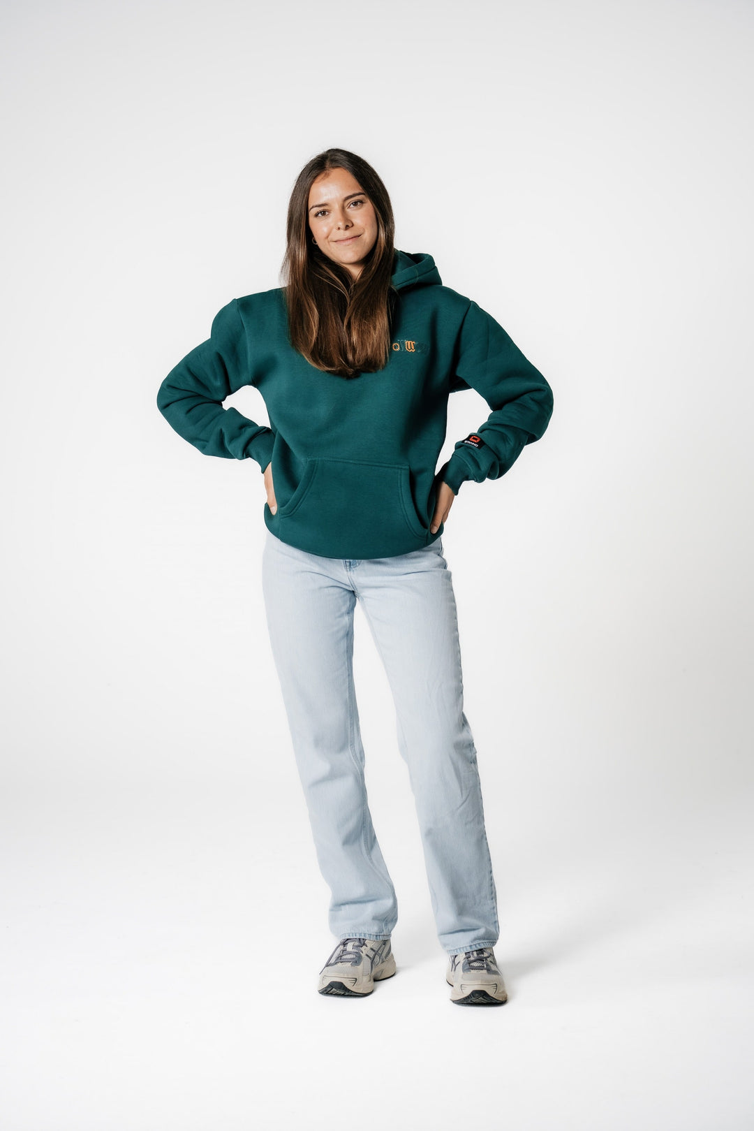 Model lächelt und trägt den dunkelgrünen POWWOW Signature Hoodie GREEN mit Kängurutasche und Händen in der Hüfte.