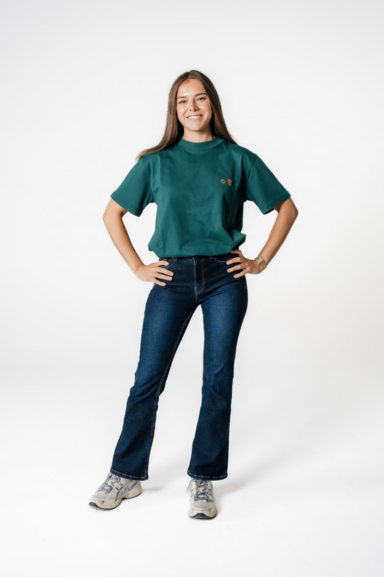 Model steht mit Händen in der Hüfte und trägt das POWWOW Classic Logo T-Shirt in GREEN (Teal) mit kleinem Logo-Stick auf der Brust.