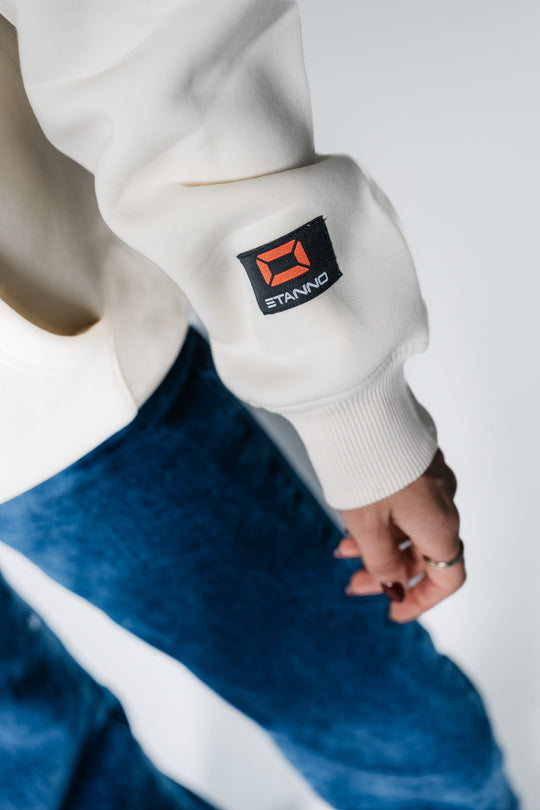 Detailaufnahme des Ärmels am POWWOW Hoodie CREAM, zeigt das schwarze Co-Branding Logo-Patch von Stanno.
