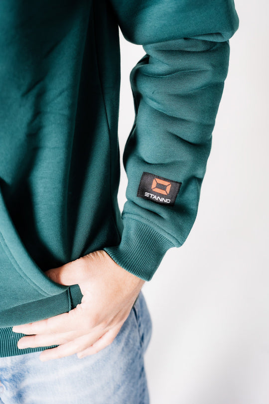 Detailaufnahme des Ärmels am dunkelgrünen POWWOW Hoodie GREEN, zeigt das schwarze Co-Branding Logo-Patch von Stanno.